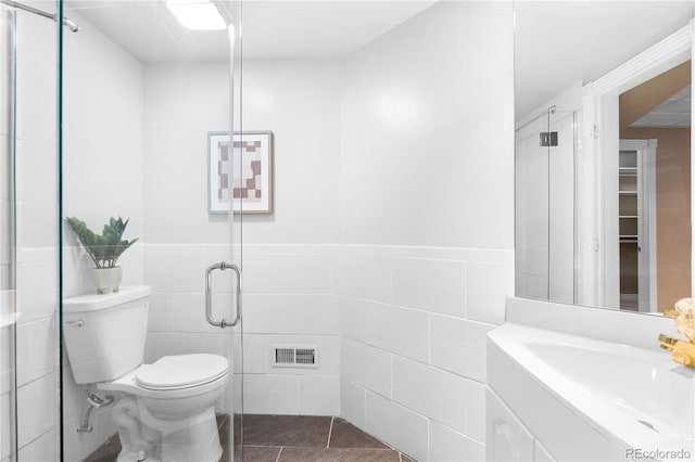 bathroom with tile patterned floors, toilet, vanity, a shower with shower door, and tile walls