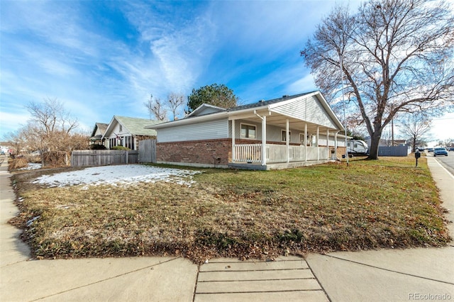 view of side of home featuring covered porch, brick siding, fence, and a lawn