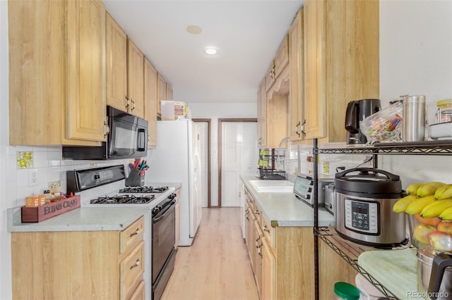 kitchen featuring tasteful backsplash, light countertops, gas stove, a sink, and black microwave