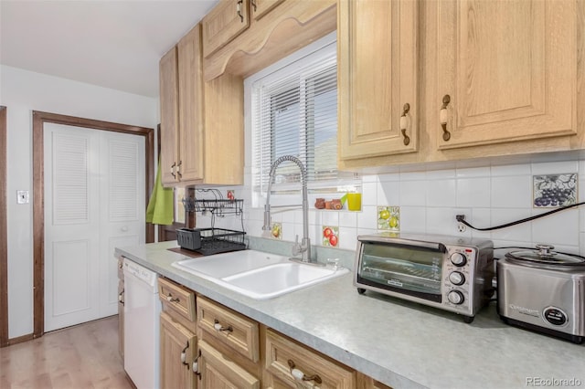 kitchen featuring white dishwasher, a toaster, a sink, light countertops, and tasteful backsplash