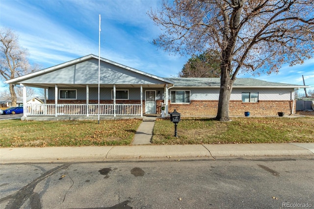 view of front of house with a front yard, covered porch, and brick siding