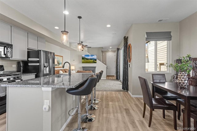 23534 E 5th Pl, Aurora, CO 80018 - kitchen featuring stainless steel appliances, light wood-style floors, a ceiling fan, a fireplace, and light stone counters