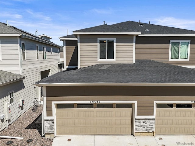 23534 E 5th Pl, Aurora, CO 80018 - rear view of property with roof with shingles, a garage, driveway, and stone siding