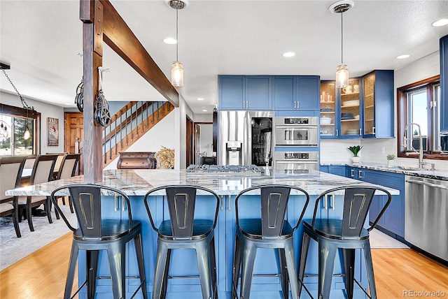 1567 Tapadero Rd, Bailey, CO 80421 - kitchen featuring blue cabinets, stainless steel appliances, light stone counters, a breakfast bar, and glass insert cabinets