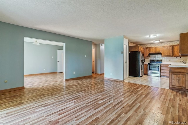 kitchen with appliances with stainless steel finishes, brown cabinets, under cabinet range hood, light wood-style floors, and light countertops