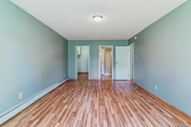 unfurnished bedroom with a baseboard radiator, light wood-type flooring, baseboards, and a spacious closet