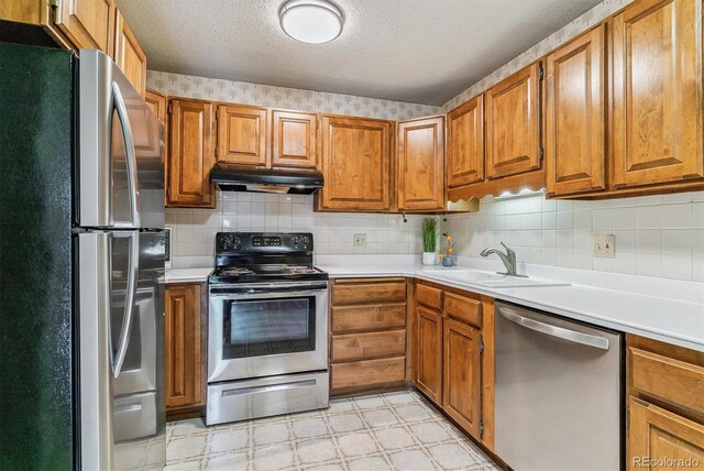 13626 E Bates Ave Unit 110, Aurora, CO 80014 - kitchen with appliances with stainless steel finishes, under cabinet range hood, a sink, brown cabinetry, and light floors