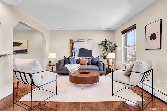 living room featuring arched walkways, recessed lighting, a baseboard heating unit, wood finished floors, and baseboards