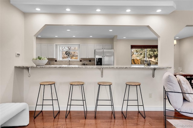 kitchen with backsplash, stainless steel refrigerator with ice dispenser, a kitchen breakfast bar, and wood finished floors