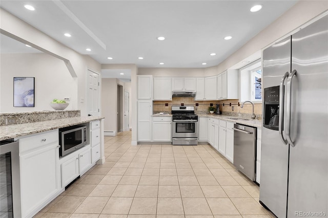 kitchen with stainless steel appliances, backsplash, white cabinets, beverage cooler, and under cabinet range hood