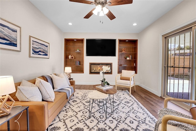 living area featuring baseboards, a ceiling fan, a glass covered fireplace, wood finished floors, and recessed lighting