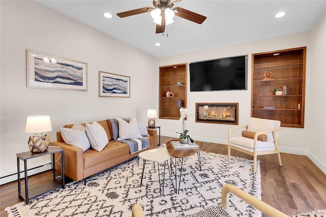 living room with baseboards, a glass covered fireplace, a baseboard radiator, wood finished floors, and recessed lighting