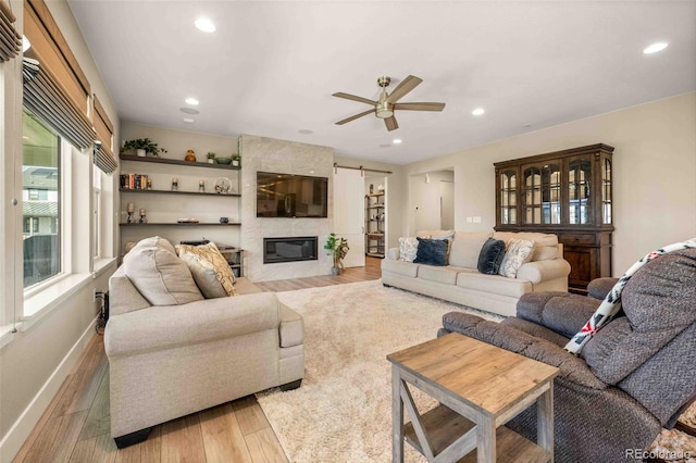 living room with a barn door, ceiling fan, a fireplace, and light hardwood / wood-style floors