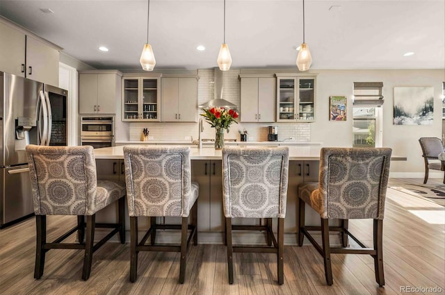 kitchen featuring wall chimney exhaust hood, decorative backsplash, stainless steel appliances, and an island with sink