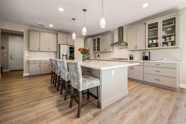 kitchen featuring wall chimney range hood, a kitchen breakfast bar, stainless steel fridge with ice dispenser, gray cabinets, and a kitchen island with sink