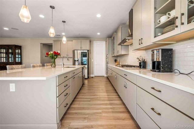 kitchen featuring tasteful backsplash, sink, hanging light fixtures, and wall chimney range hood