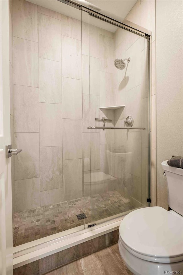 bathroom with wood-type flooring, toilet, and a shower with door