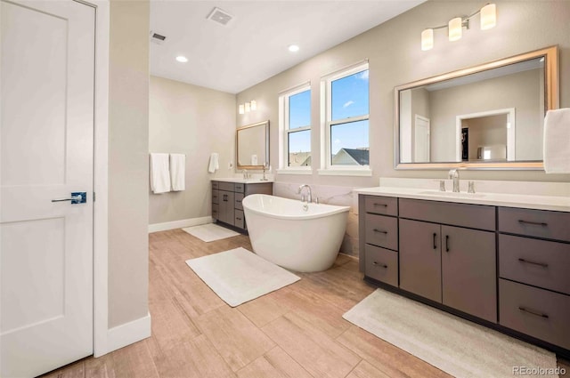 full bathroom featuring a freestanding tub, wood finished floors, two vanities, a sink, and visible vents