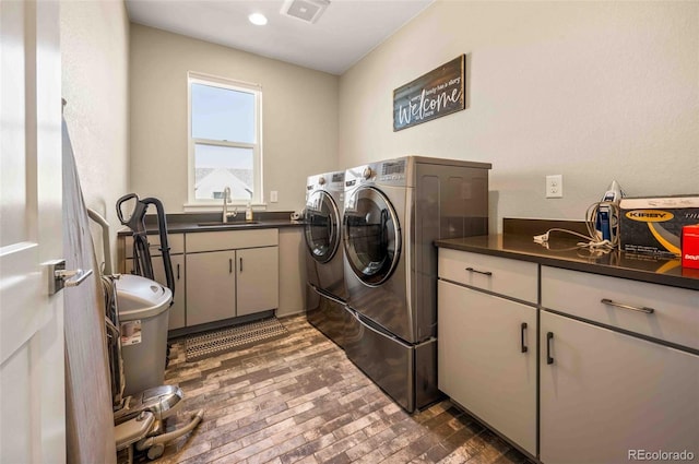 laundry area featuring brick floor, cabinet space, visible vents, a sink, and separate washer and dryer