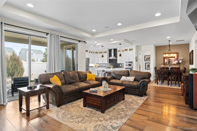 living room featuring a notable chandelier, light hardwood / wood-style flooring, and a raised ceiling