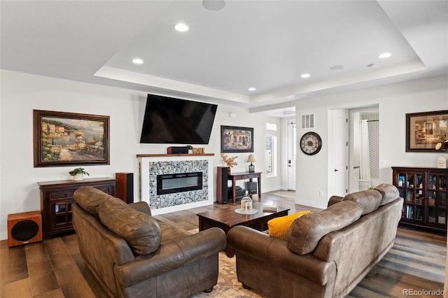 living room featuring dark wood-type flooring, a fireplace, and a raised ceiling