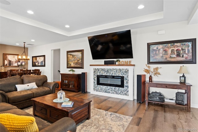 living room featuring an inviting chandelier, wood-type flooring, a tiled fireplace, and a raised ceiling