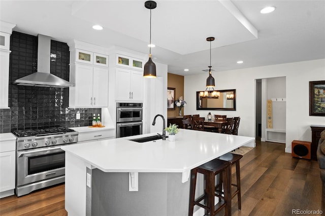 kitchen with sink, an island with sink, wall chimney exhaust hood, and appliances with stainless steel finishes