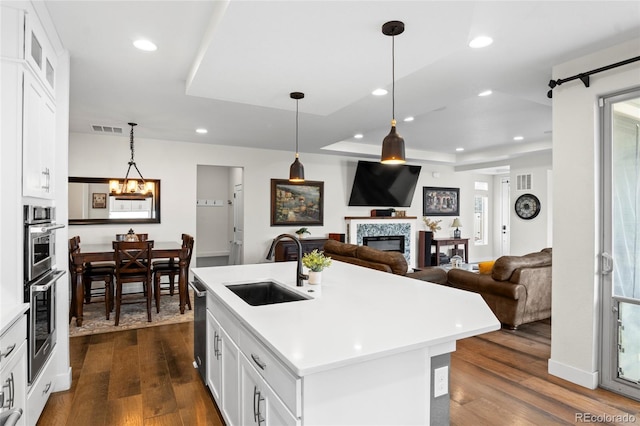 kitchen with sink, hanging light fixtures, dark hardwood / wood-style floors, an island with sink, and white cabinets