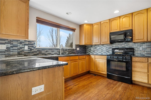 kitchen with sink, tasteful backsplash, light hardwood / wood-style flooring, dark stone countertops, and black appliances