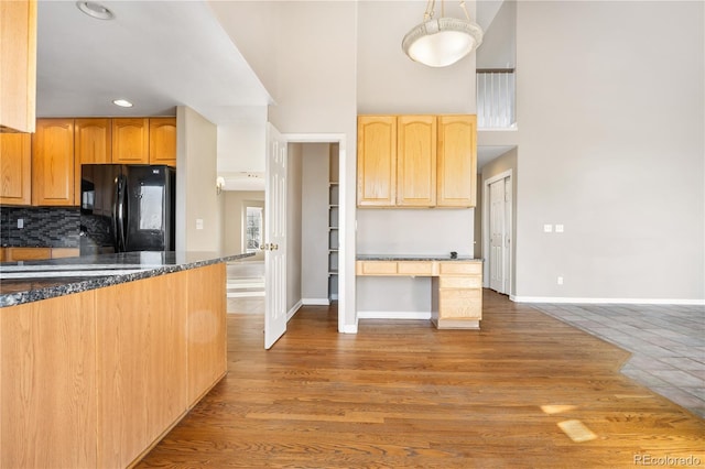 kitchen featuring dark stone counters, black fridge, hanging light fixtures, hardwood / wood-style flooring, and decorative backsplash