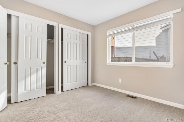 unfurnished bedroom featuring light carpet and multiple closets