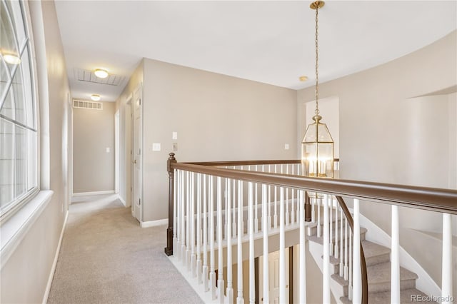 hall featuring light carpet and a notable chandelier