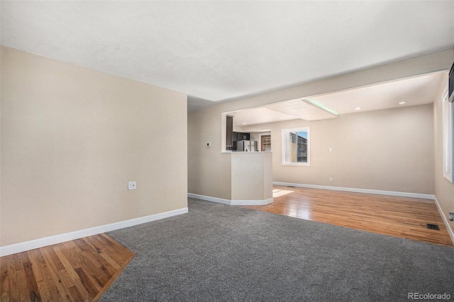 unfurnished living room featuring carpet, visible vents, baseboards, and wood finished floors