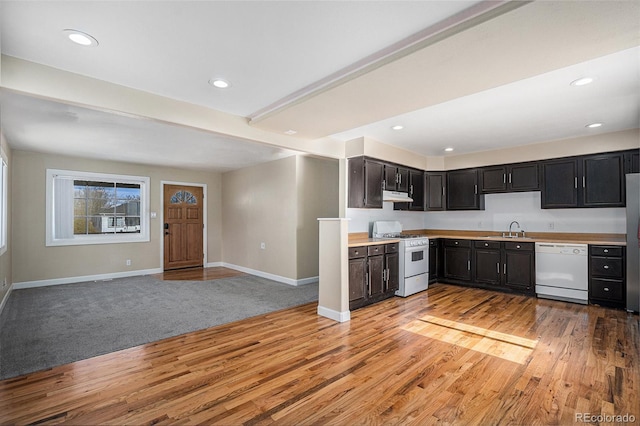 kitchen featuring light countertops, a sink, white appliances, under cabinet range hood, and baseboards