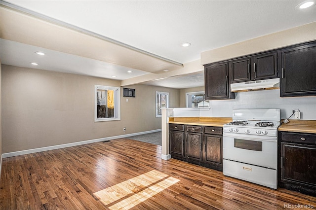 kitchen featuring baseboards, dark wood finished floors, light countertops, under cabinet range hood, and gas range gas stove