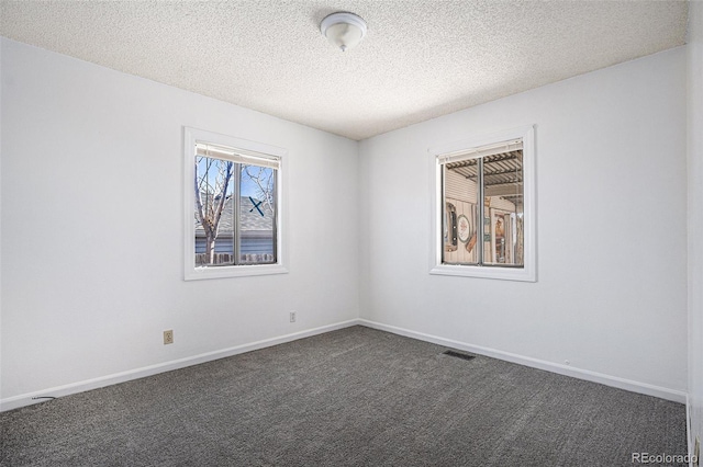 spare room featuring baseboards, visible vents, dark colored carpet, and a textured ceiling