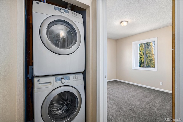 clothes washing area with a textured ceiling, stacked washer and dryer, laundry area, baseboards, and carpet