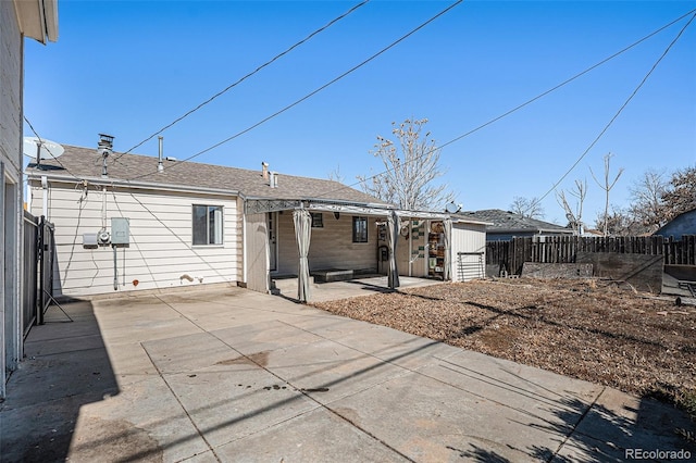 rear view of house featuring a shingled roof, a patio area, and fence