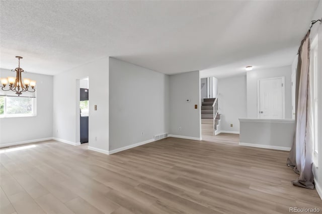 1005 S Lewiston Way, Aurora, CO 80017 - unfurnished living room featuring a chandelier, light wood-style flooring, stairway, baseboards, and a textured ceiling