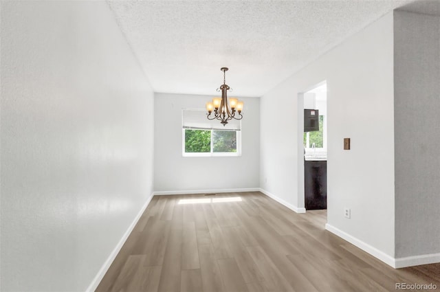 1005 S Lewiston Way, Aurora, CO 80017 - unfurnished dining area with a chandelier, wood finished floors, baseboards, and a textured ceiling