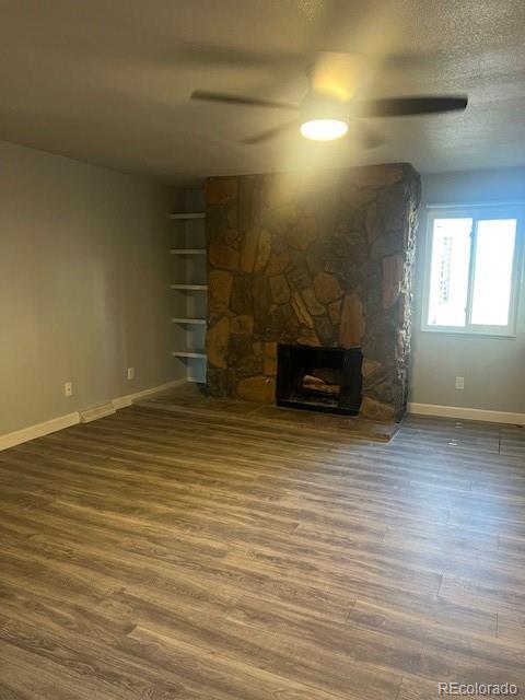 unfurnished living room with ceiling fan, a fireplace, dark hardwood / wood-style floors, and a textured ceiling