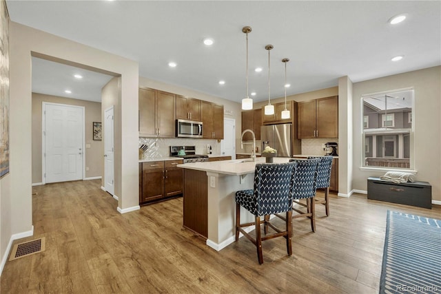 kitchen with pendant lighting, a breakfast bar, appliances with stainless steel finishes, light hardwood / wood-style floors, and a center island with sink