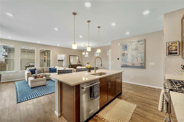 kitchen featuring appliances with stainless steel finishes, decorative light fixtures, sink, a kitchen island with sink, and light hardwood / wood-style flooring