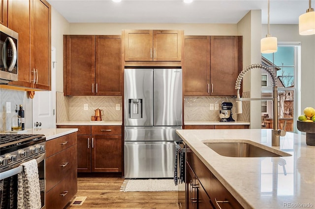 kitchen featuring appliances with stainless steel finishes, pendant lighting, sink, light stone countertops, and light wood-type flooring