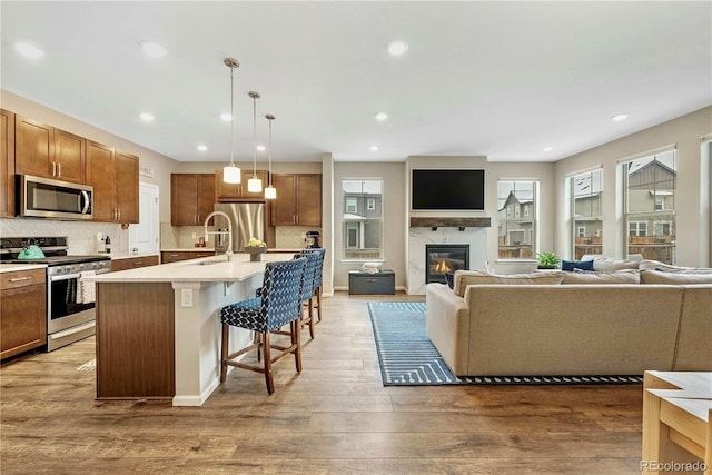 kitchen with a kitchen bar, stainless steel appliances, a center island with sink, pendant lighting, and a healthy amount of sunlight