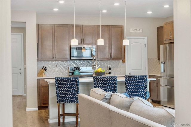 kitchen with decorative light fixtures, a kitchen bar, decorative backsplash, stainless steel appliances, and light hardwood / wood-style flooring