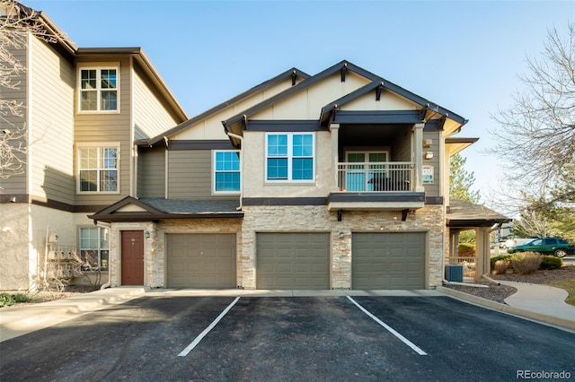 view of property with a garage, stone siding, a balcony, and driveway