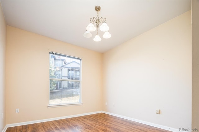 unfurnished room with wood finished floors, a healthy amount of sunlight, baseboards, and a chandelier