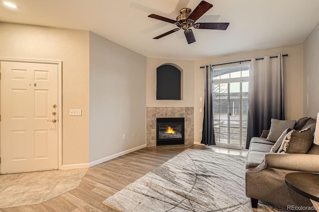 living area featuring a ceiling fan, a fireplace, light wood-style flooring, and baseboards