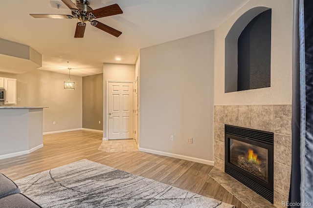 unfurnished living room with ceiling fan, light wood-type flooring, a fireplace, and baseboards